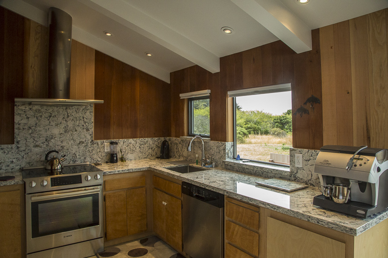 A kitchen showing the counter with sink, coffee maker, and stove with a view of the garden through a window.