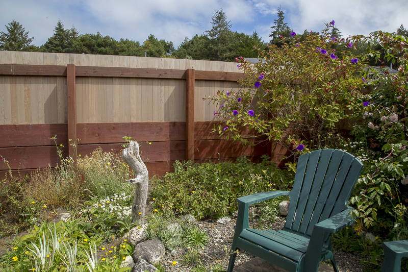 The interior of a fenced garden with flowers and a green chair.