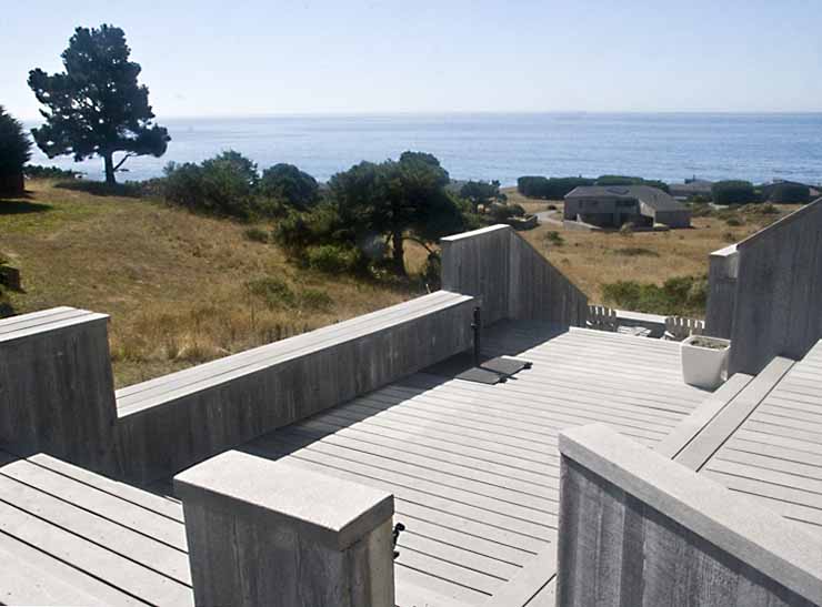 An exterior deck with a view of the ocean beyond the hillside.