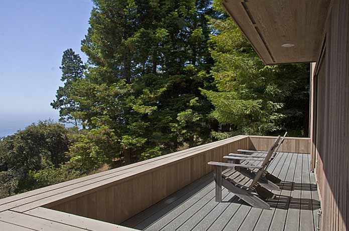 The finished deck with two chairs looking out past some trees to the ocean beyond.