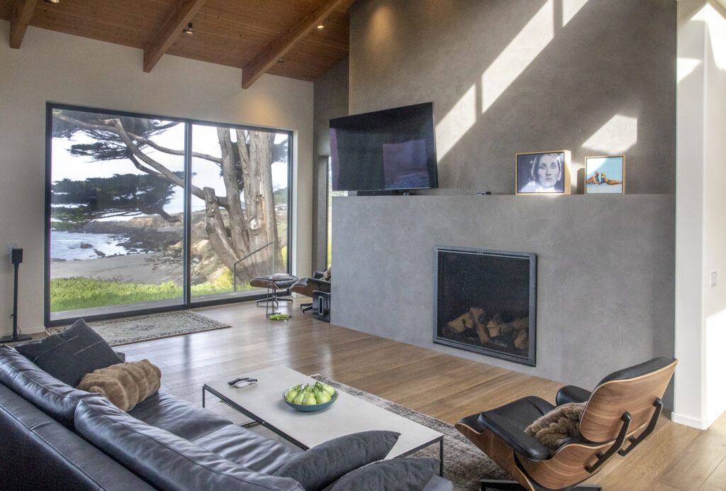 Interior of a room with sofa, chair, fireplace and view of the garden out a large window,