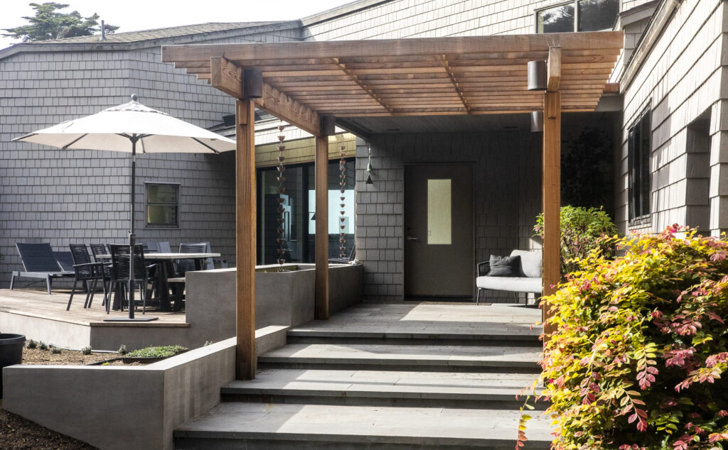 Exterior of a home with stairs, a portico, an umbrella and several chairs.